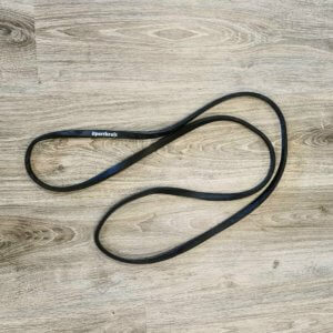 Musta Sportkraft-vastuskuminauha puulattialla, korostettuna luonnonvalossa treeniä varten.