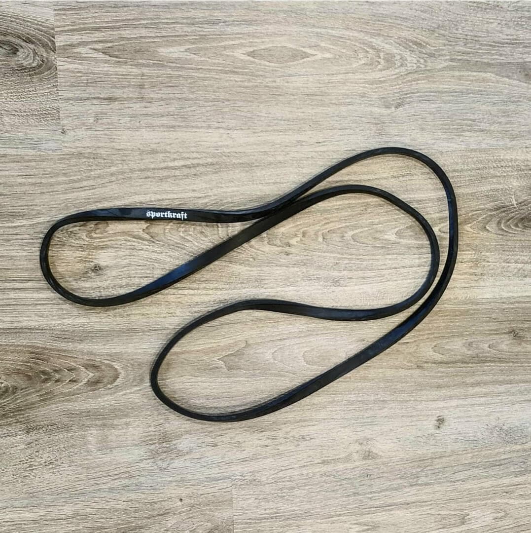 Musta Sportkraft-vastuskuminauha puulattialla, korostettuna luonnonvalossa treeniä varten.