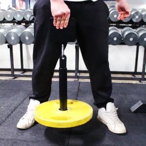 Henkilö kuntosalilla pitelee keltaista Sportkraft-lisäpainoankkuria voimaharjoittelua varten.