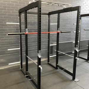 Musta HC Pro Power Rack kuntosalilla, säädettävät tangonpidikkeet ja punaiset Olympic-lukot.