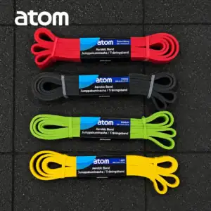 Neljä eriväristä Atom vastuskuminauha, Neljä eri väriä, (Extra Heavy punainen, Heavy musta, Medium vihreä ja Light keltainen) asetettuna kuntosalin lattialle.