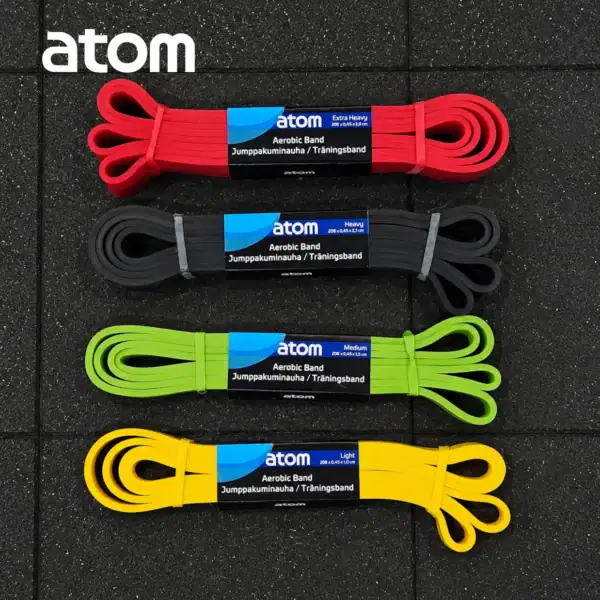 Neljä eriväristä Atom vastuskuminauha, Neljä eri väriä, (Extra Heavy punainen, Heavy musta, Medium vihreä ja Light keltainen) asetettuna kuntosalin lattialle.
