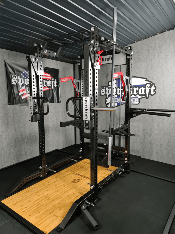SportKraft power rack kuntosalilla, musta metallirakenne ja puinen nostolava voimaharjoitteluun.
