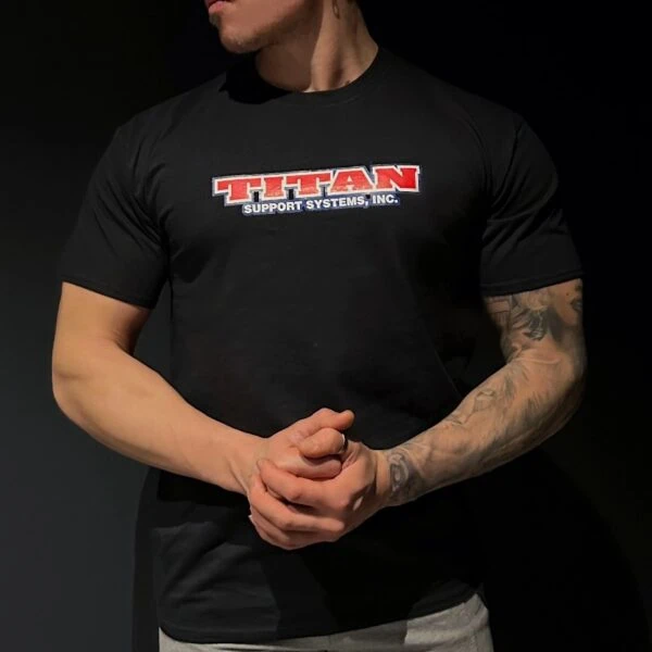 Sportkraft - Salimarkku Oy 27 Lihaksikas mies mustassa Titan Support Systems -paidassa tummalla taustalla.