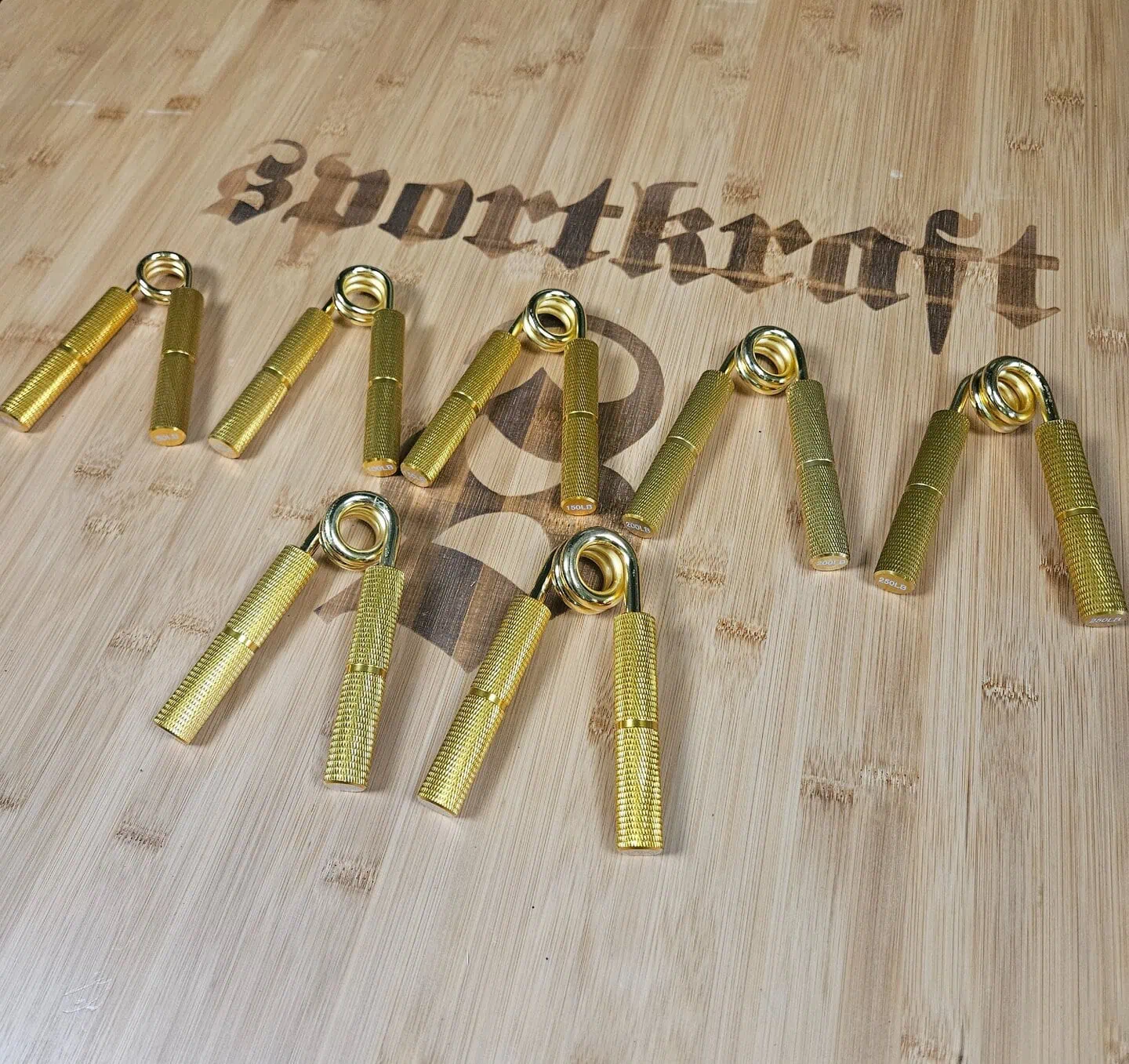 Kultaiset painonnostokoukut vaalealla puupinnalla, Sportkraft-logo taustalla.