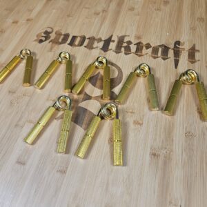 Kultaiset painonnostokoukut vaalealla puupinnalla, Sportkraft-logo taustalla.