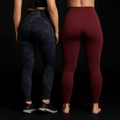 Kaksi urheilullista naista tyylikkäissä leggingseissä mustaa taustaa vasten